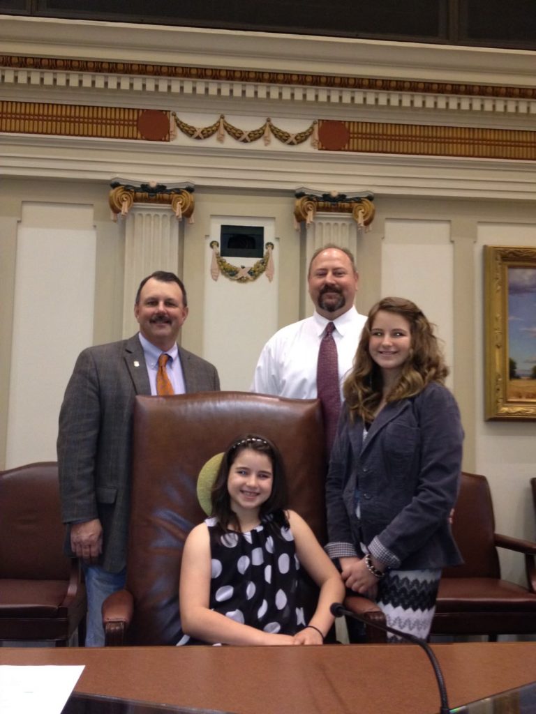 Ten-year-old Hailey Wallace (seated) poses with her father in the House Chambers when he was first sworn in as a State Representative in 2014. Pictured (standing, left to right): former Representative Don Arms (R-District 63), Representative Kevin Wallace (R-District 32) and Ashlynn Wallace.