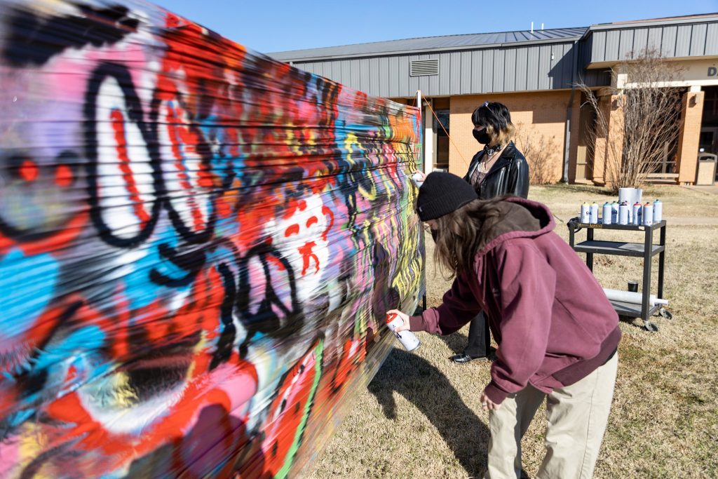 Two members of the SSC Art Club Paint at one of their graffiti tag stations set up during the college’s 48th annual Interscholastic Meet on March 24.