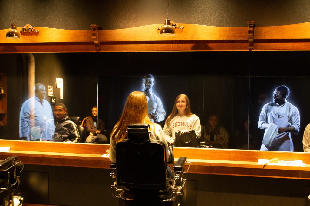 Cepado Wilkins, Jr. (left), of Shawnee, and Sydney Winchester (right), of Prague, sit in a barbershop re-creation and listen to holographic actors describe life in Greenwood before violence broke out.