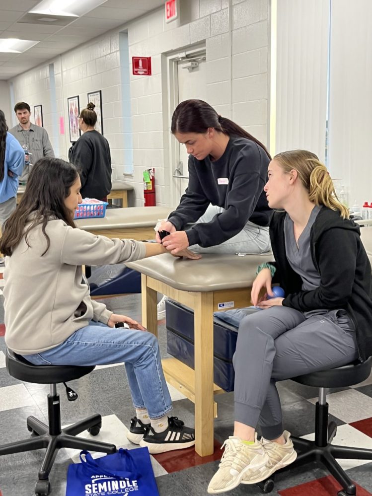 PTA students Paige Risenhoover (center) and Megan Whited (right) discuss the application of Kinesio Tape to prospective student Monse Ortiz from Shawnee High School.
