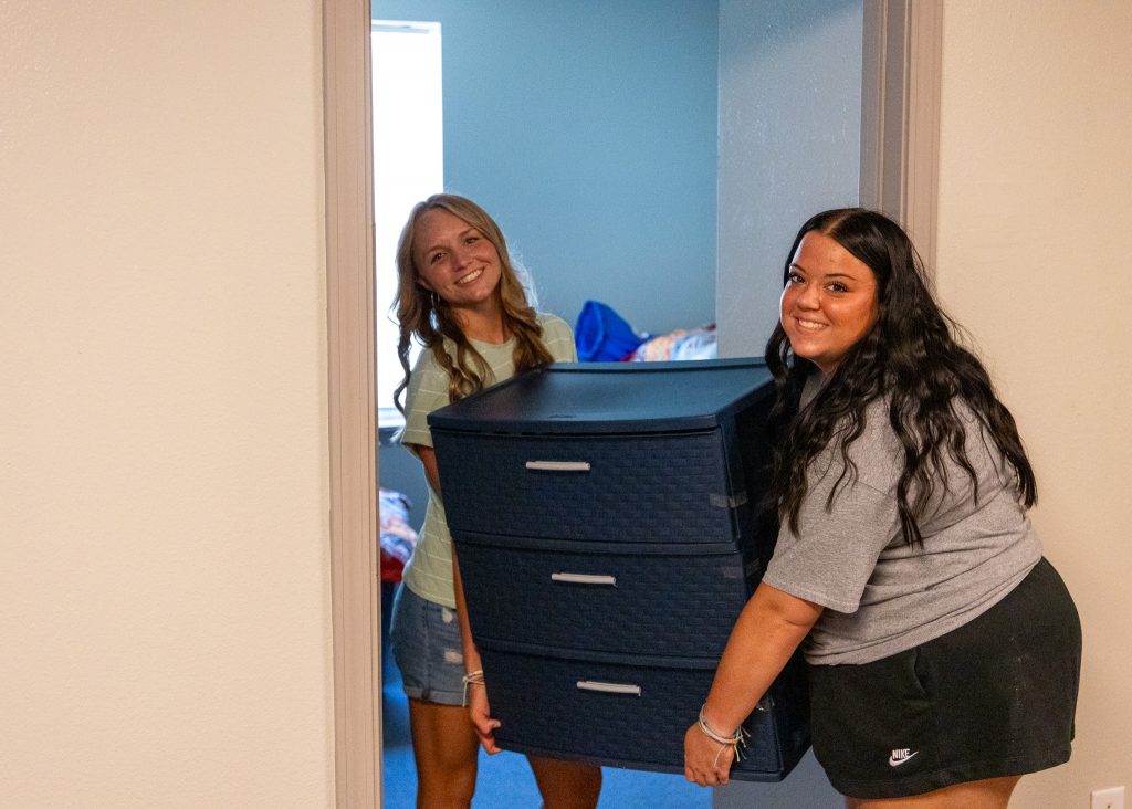 Olivia Sander (right) lends a hand as incoming freshman Jaylee Friend (left) of Prague moves into her dorm.