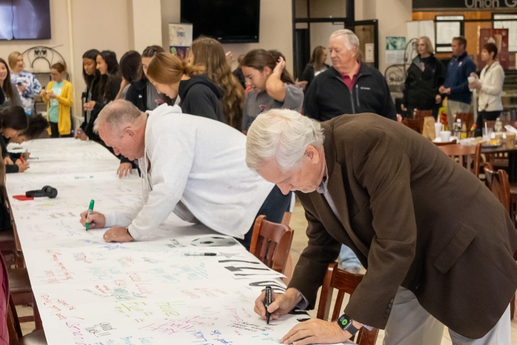 Prior to the event, soccer supporters Ernie Willis (left) and Mark Schell (right) signed a banner encouraging the team.