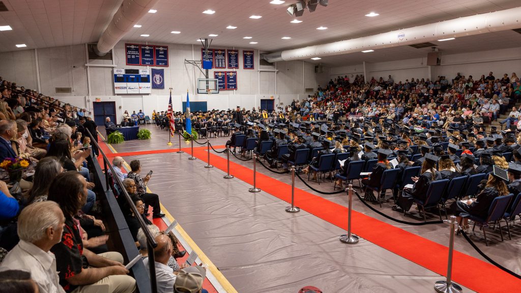In this photo, a large crowd is shown seated in the Raymond Harber Field house as graduates, faculty and staff, fill the floor seating.