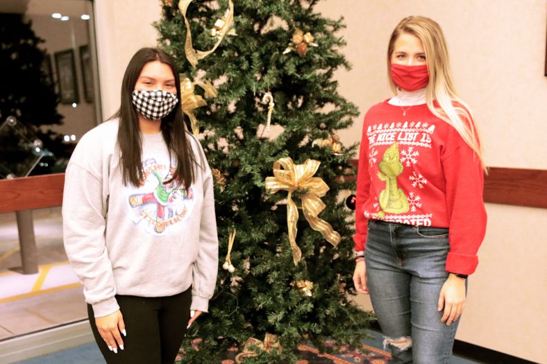 Two students stand by Christmas tree.