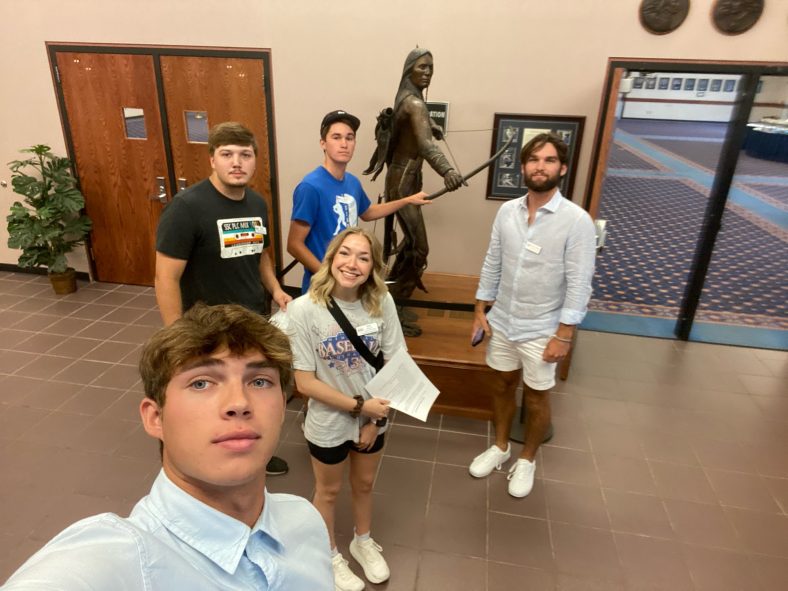 Group of students pose in front of statue