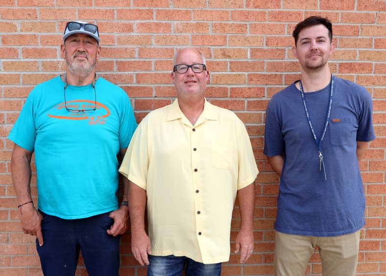 three men pose against brick wall