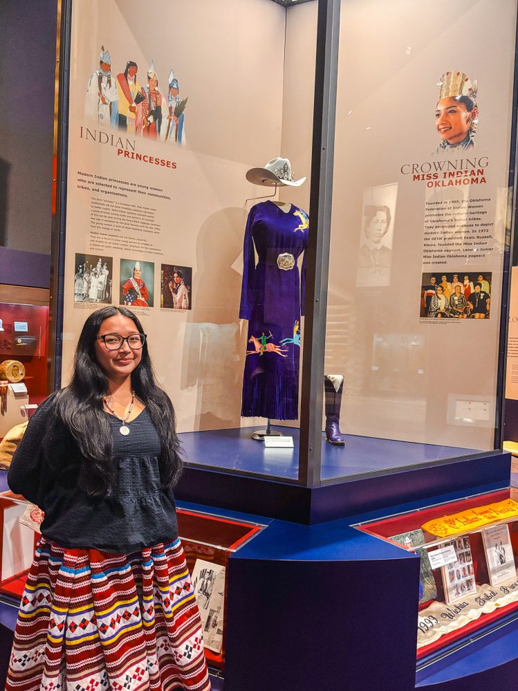 In this photo, Seminole State College freshman Alivia Wapskineh, 2025 Miss Seminole Nation, stands in front of the Indian Princesses exhibit at the Oklahoma History Center during the 2026 George and Donna Nigh Leadership Academy in Oklahoma City.