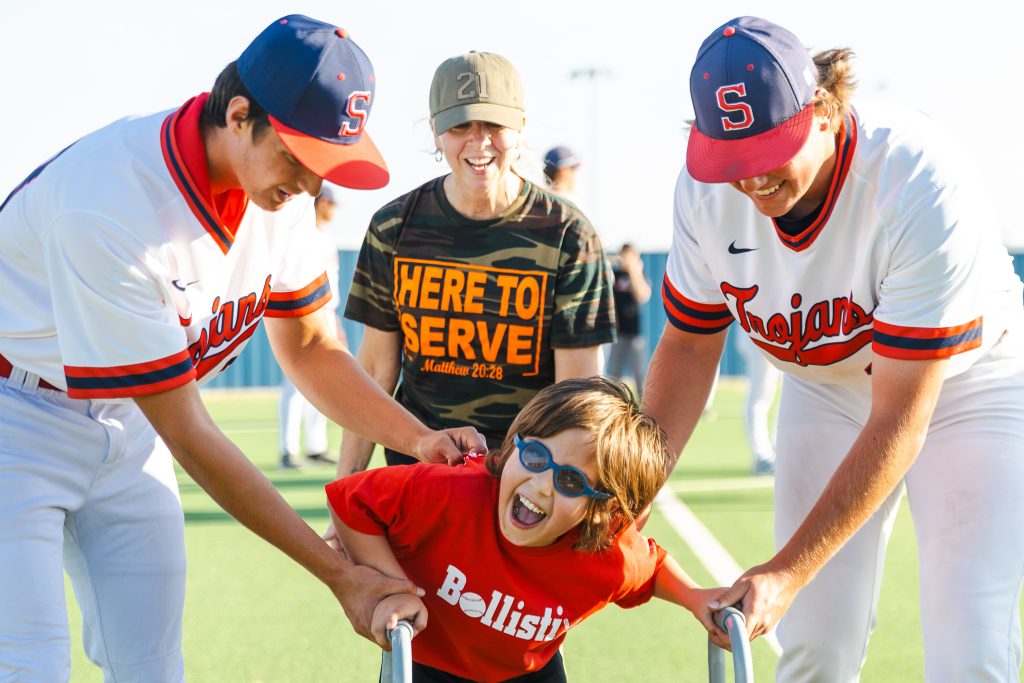 Andrew Taber of Bethany, left, A League of Their Own Director Holli Daniels, back center, and Ethan Rich of Prague, right, cheer on Alex Tilley of Seminole as he rounds third 