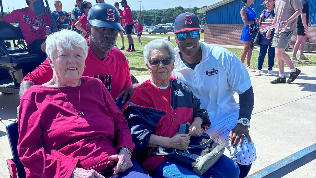 In this photo, Long-time SSC food service director Bonnie Ritchie and cafeteria worker Polly Wells pose for a photo with Trojans Assistant Coach James Martin and Head Coach Mack Chambers.