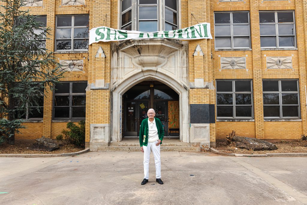 Bill Wantland, 92, stands at the old Seminole High School wearing his debate letter sweater. While completing his senior year of high school, Wantland teamed with Tommy Kelton to win the 1952 national debate championship for Seminole Junior College.